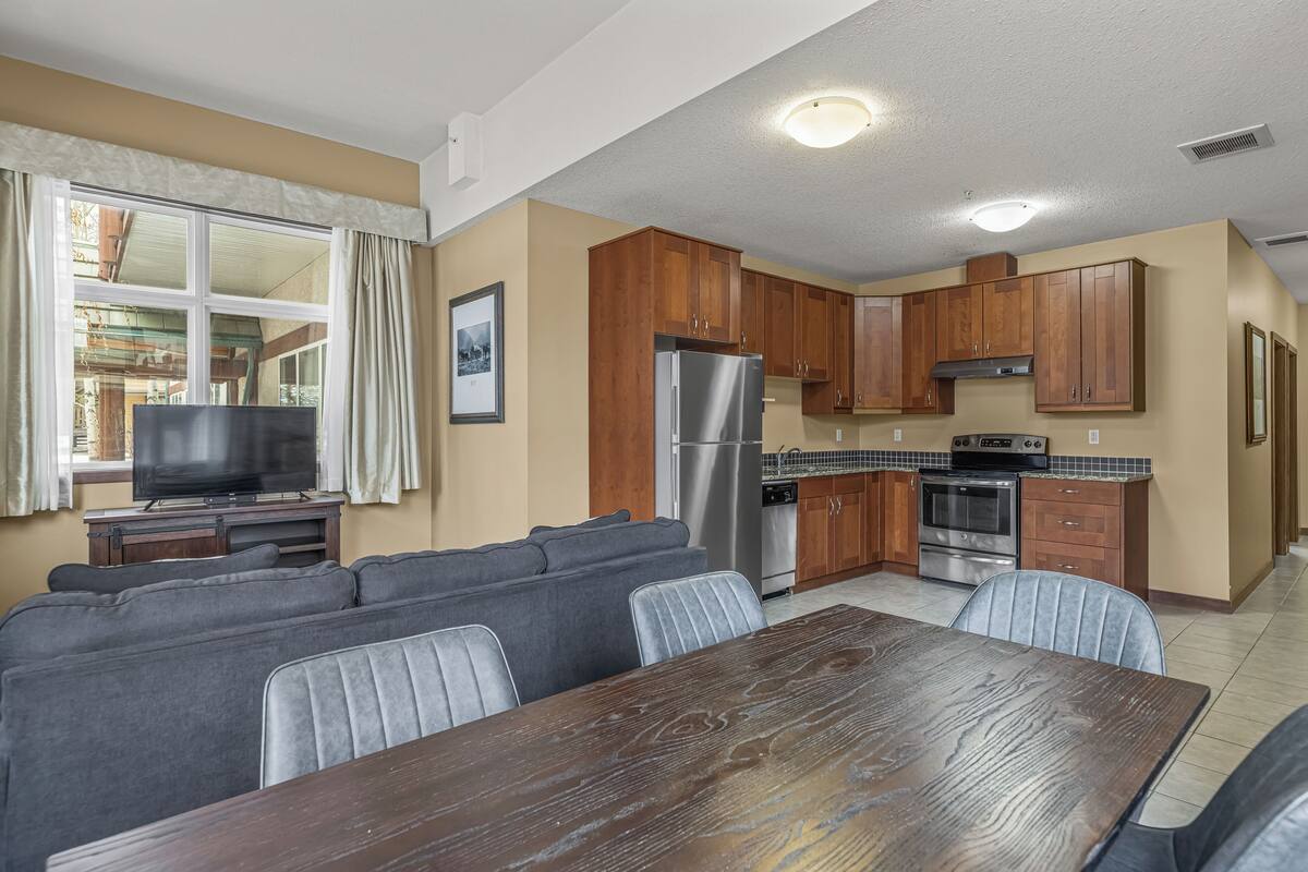 A living room with a sofa set, a dining table, a kitchen with wooden cabinets, a refrigerator, and a television.
