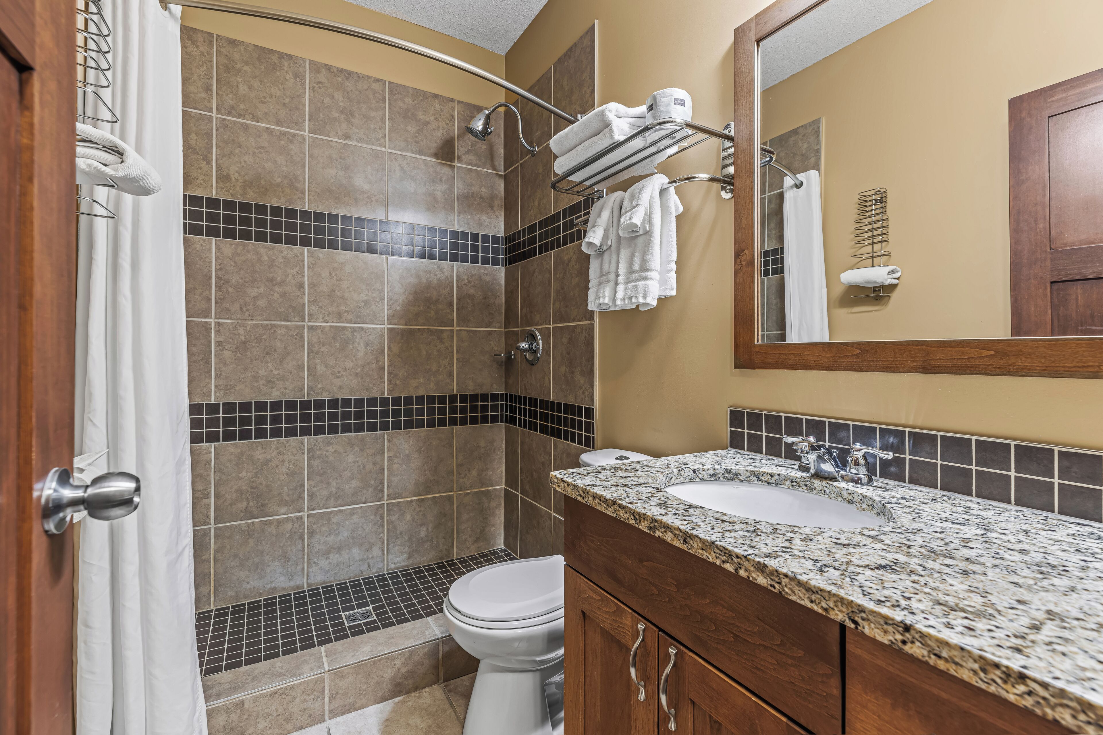 A bathroom with a shower, toilet, vanity with two sinks, and a mirror.
