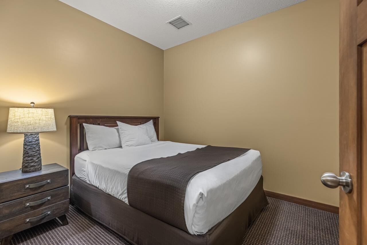 Una camera d'albergo con un letto, un comodino, una lampada e una porta.