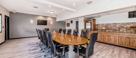 A conference room with a large oval table, black chairs, a flat-screen TV, and a wooden cabinet.