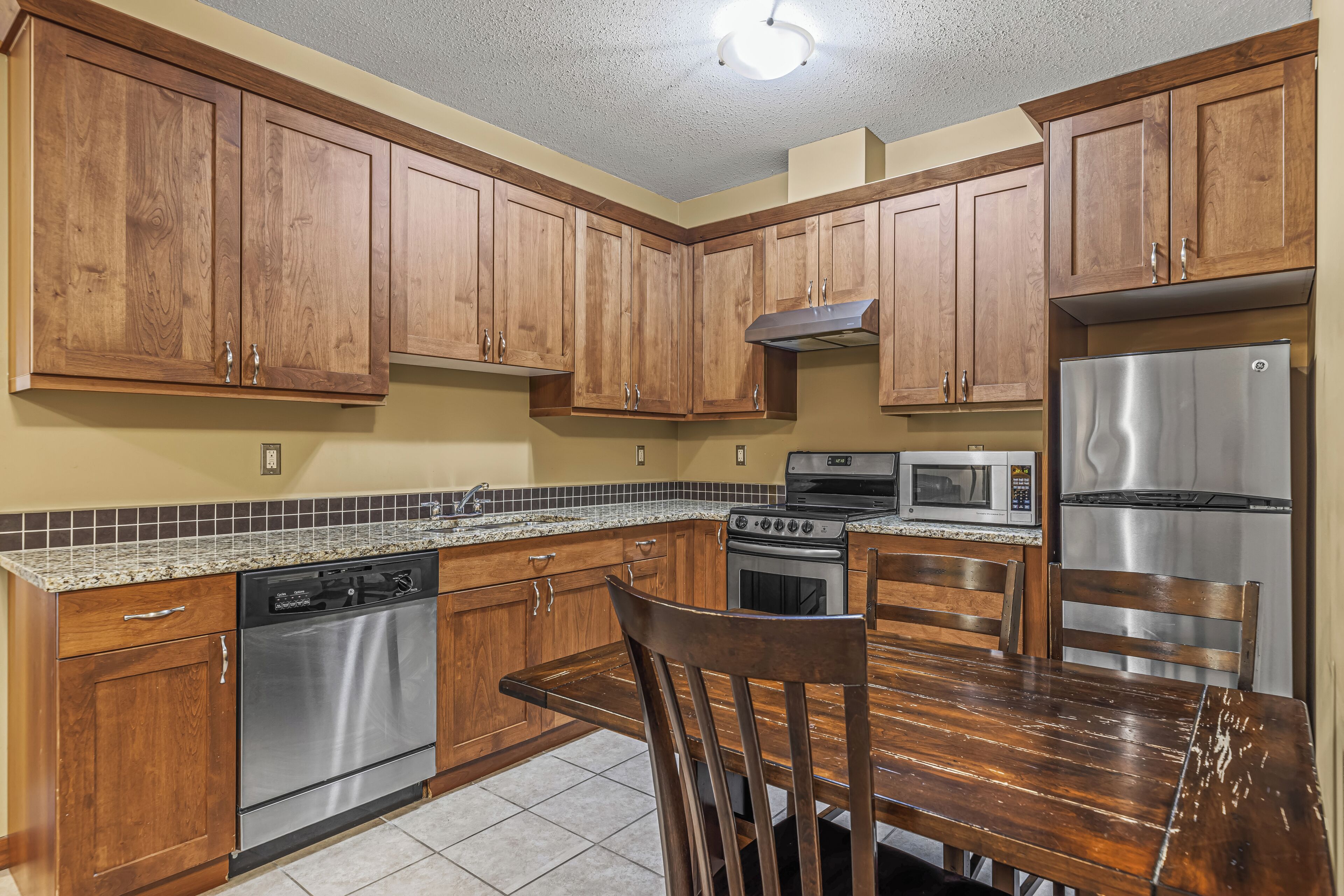 A kitchen with wooden cabinets, stainless steel appliances, a granite countertop, and a dining table with chairs.