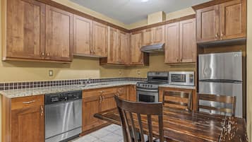 A kitchen with wooden cabinets, stainless steel appliances, a granite countertop, and a dining table with chairs.