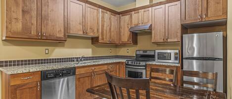 A kitchen with wooden cabinets, stainless steel appliances, a granite countertop, and a dining table with chairs.