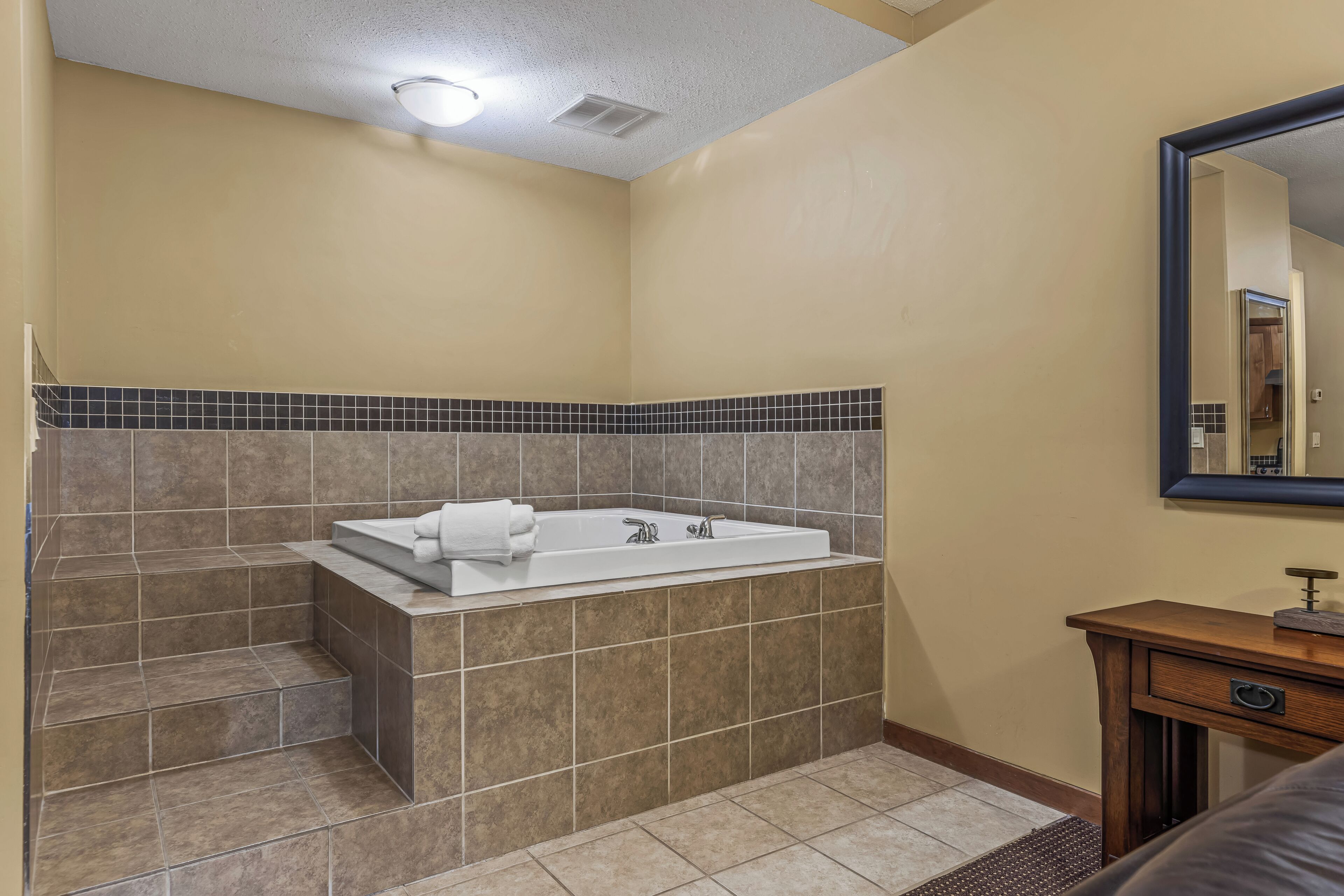 A bathroom with a bathtub, a mirror, and a wooden vanity.