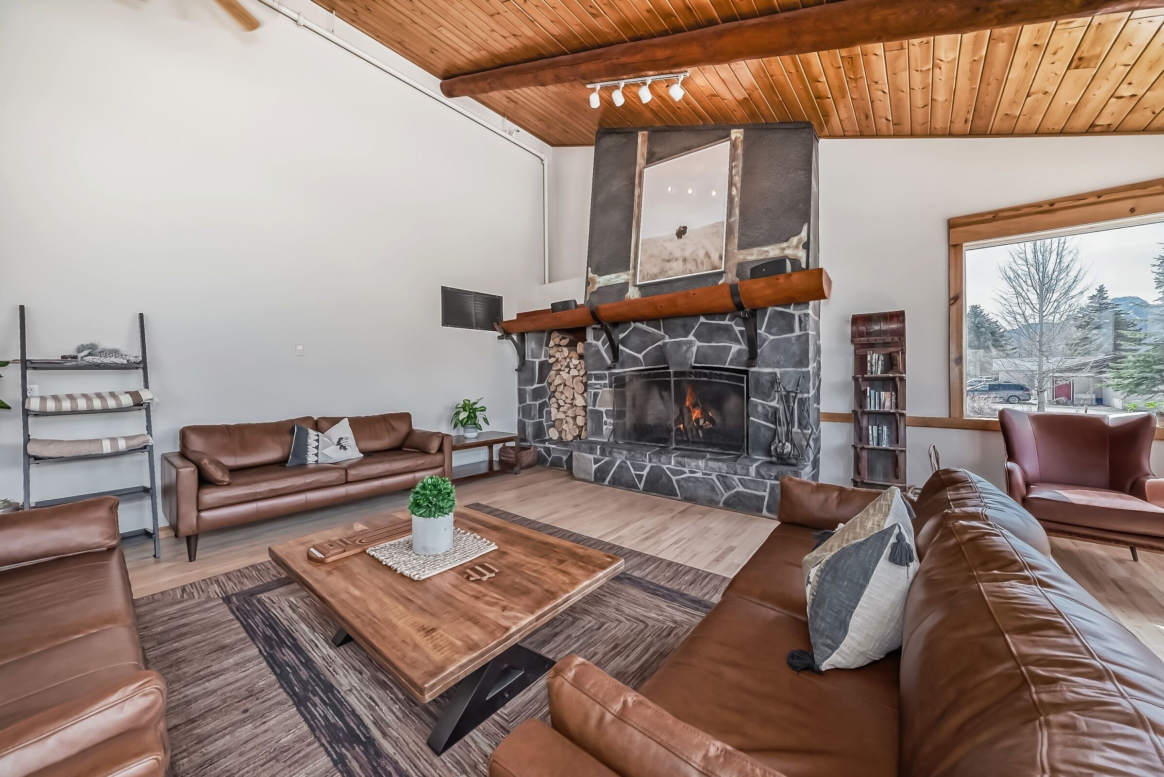 Un salon moderne avec une cheminée en pierre, des canapés en cuir et un plafond en bois.