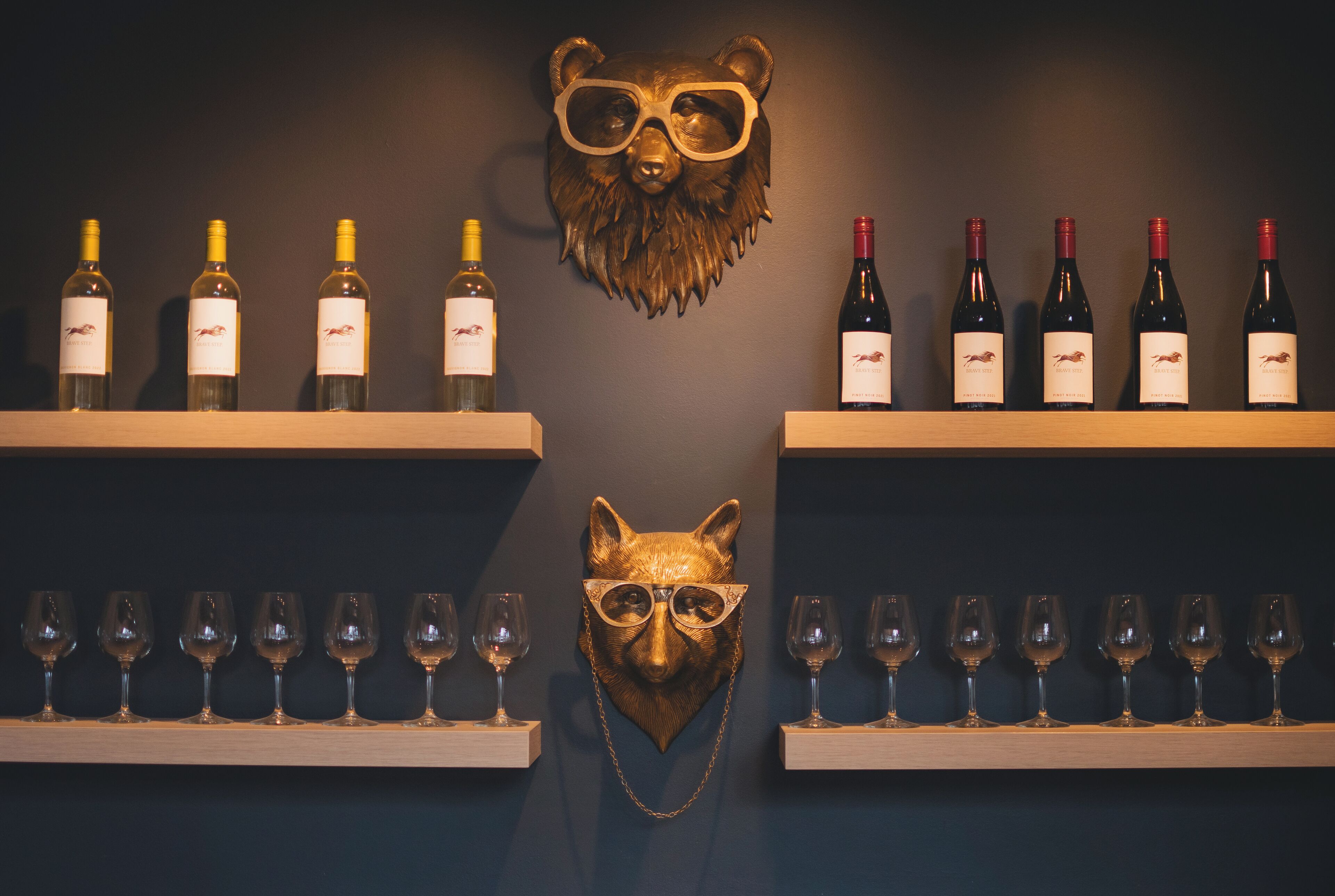 A wine display with bottles and glasses on shelves against a dark wall.
