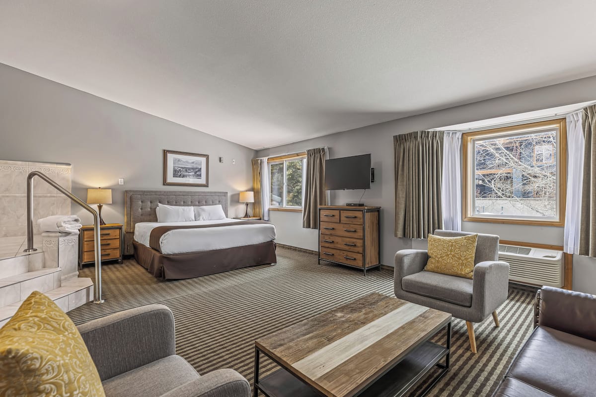 A hotel room with a bed, a desk, a chair, a TV, a dresser, and a window with curtains.
