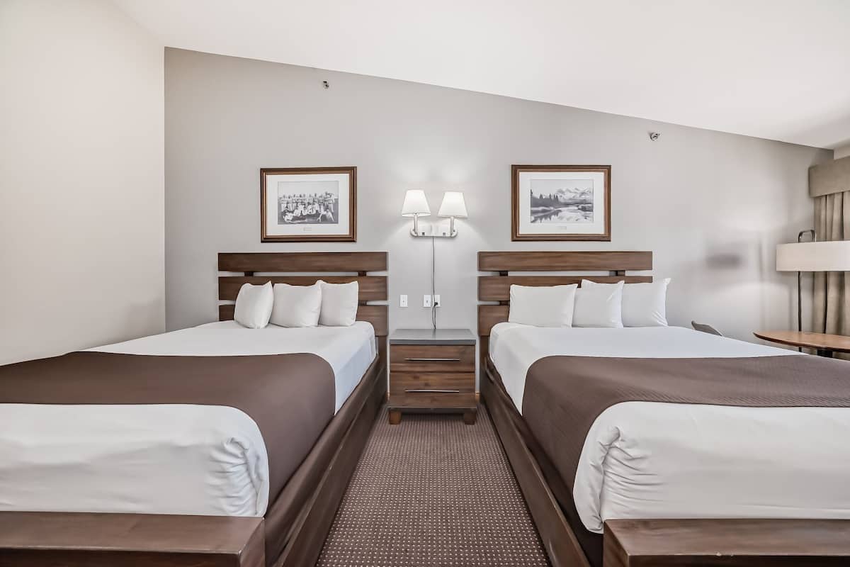 A hotel room with two beds, a small table, a lamp, and two wall-mounted lamps.