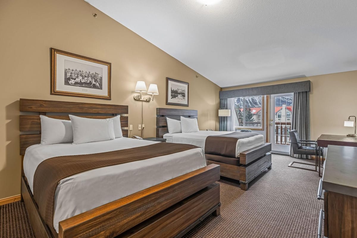 A hotel room with two beds, a desk, a chair, and a view of the outside.