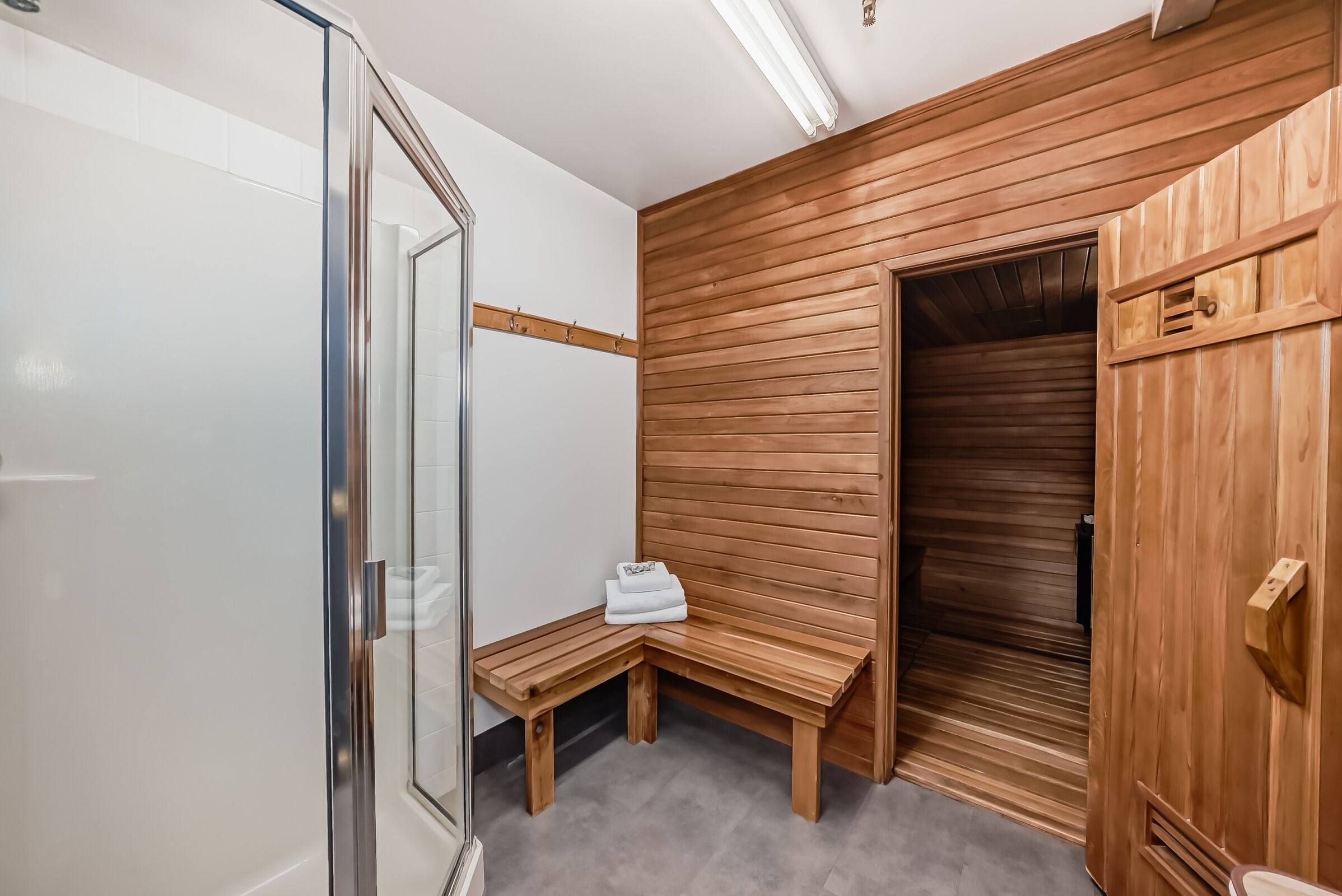 A modern bathroom with a wooden bench, a glass shower enclosure, and a wooden door.