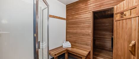 A modern bathroom with a wooden bench, a glass shower enclosure, and a wooden door.