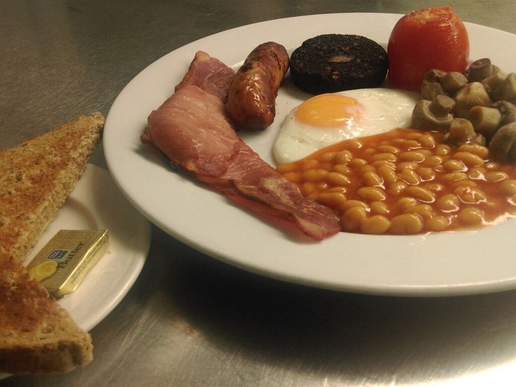 Un plato con tocino, salchichas, huevos, frijoles, champiñones, tomate y tostadas.