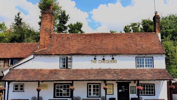 A traditional white building with a sign reading "The Chequers." It features a brick chimney, multiple windows, and outdoor seating with benches and chairs. - The Chequers Inn (Amersham)