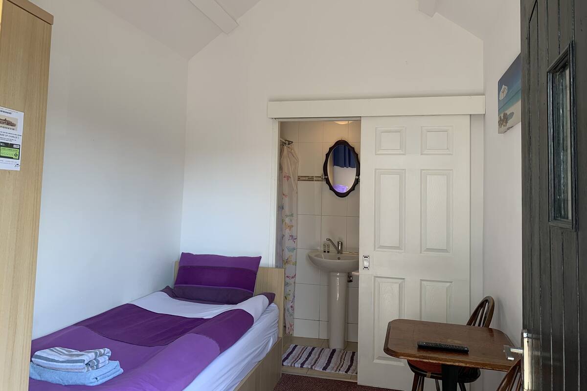 A bedroom with a bed, a small table, a chair, a sink, and a mirror.