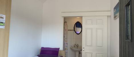 A bedroom with a bed, a small table, a chair, a sink, and a mirror.