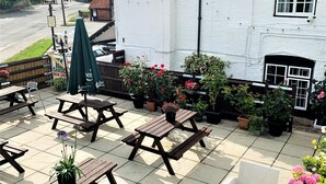 A patio area with wooden benches and tables, surrounded by potted plants and flowers. - The Chequers Inn (Amersham)