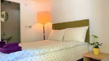 A hotel room with a bed, a bedside lamp, a small bedside table with a plant, and a bathroom visible through an open door.