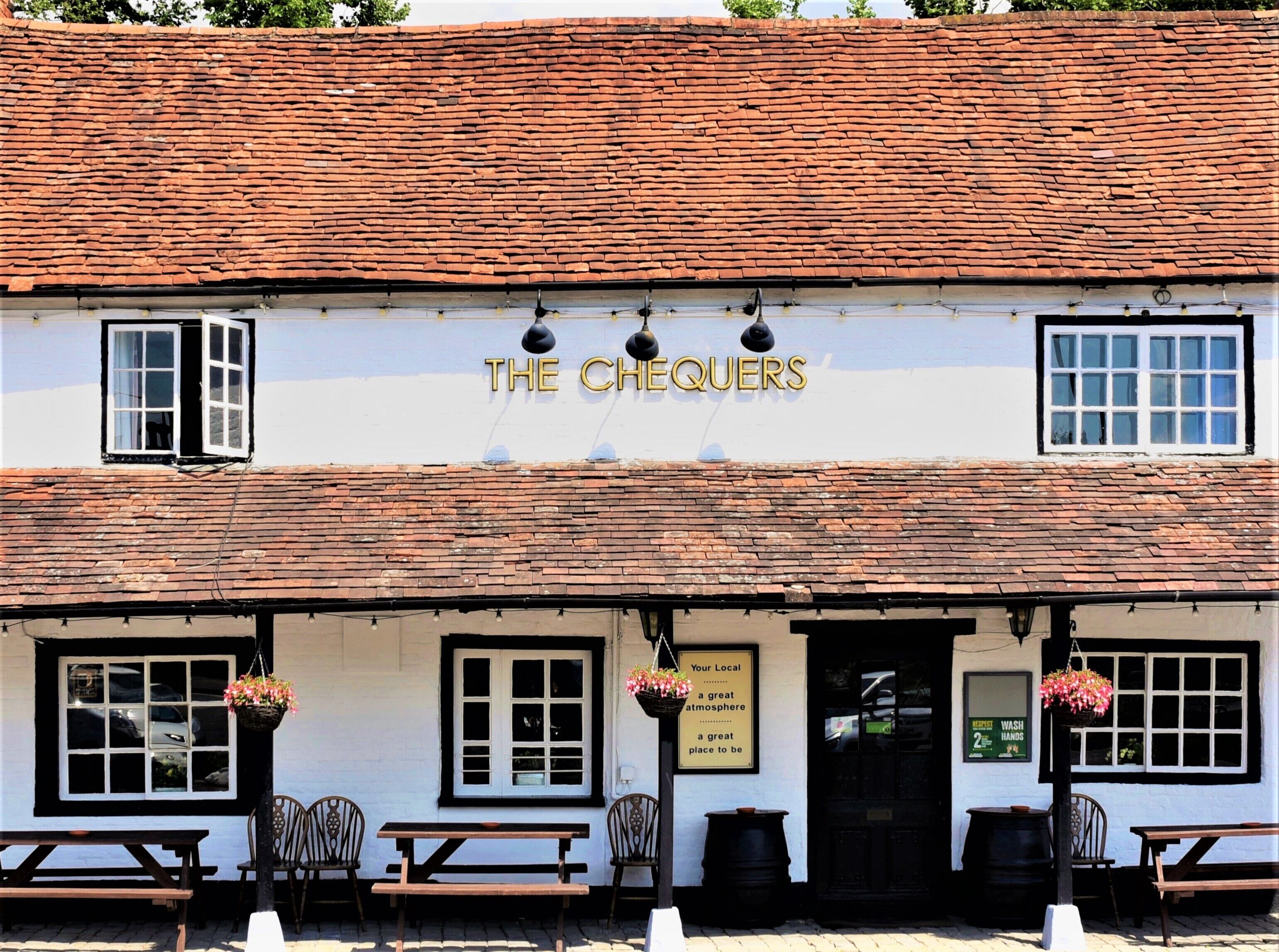 A traditional pub named "The Chequers" with a tiled roof, white exterior walls, and multiple windows. There are outdoor seating arrangements with benches and chairs.