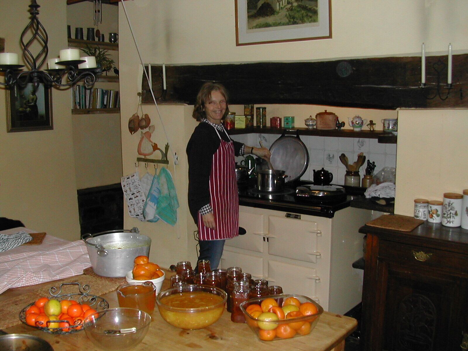 A kitchen with a person cooking, various kitchen utensils, and a table with fruits and jars.