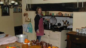 A kitchen with a person cooking, various kitchen utensils, and a table with fruits and jars.