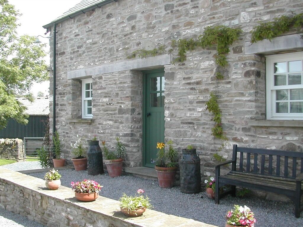 Un bâtiment en pierre avec une porte verte, des plantes en pot et un banc.
