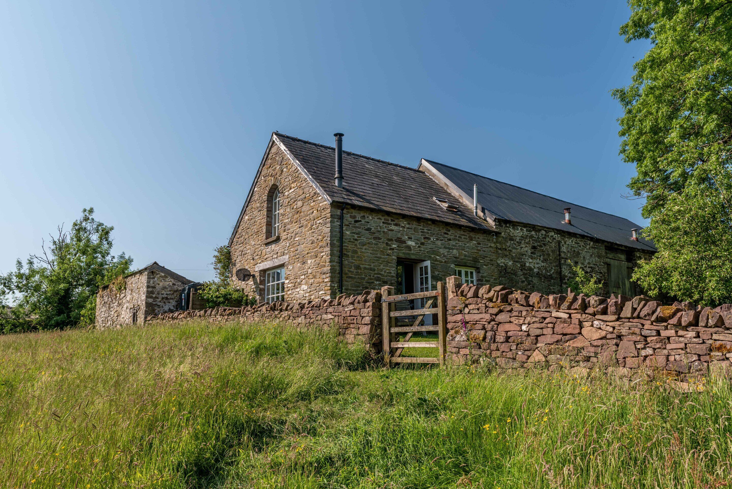 A stone farmhouse with a sloped roof, a wooden gate, and a stone wall.