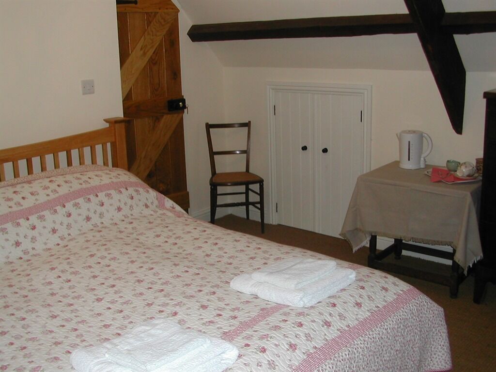 Un dormitorio con cama, una silla, una puerta y una mesa con hervidor.