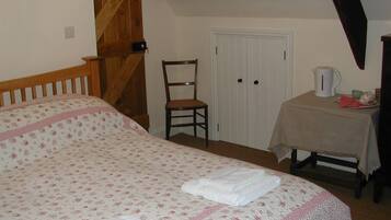 Un dormitorio con cama, una silla, una puerta y una mesa con hervidor.