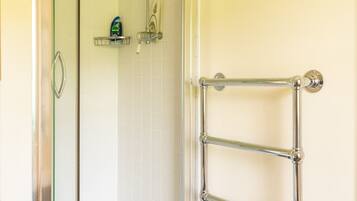 A bathroom with a glass shower enclosure, a towel rack, and a shelf with toiletries.