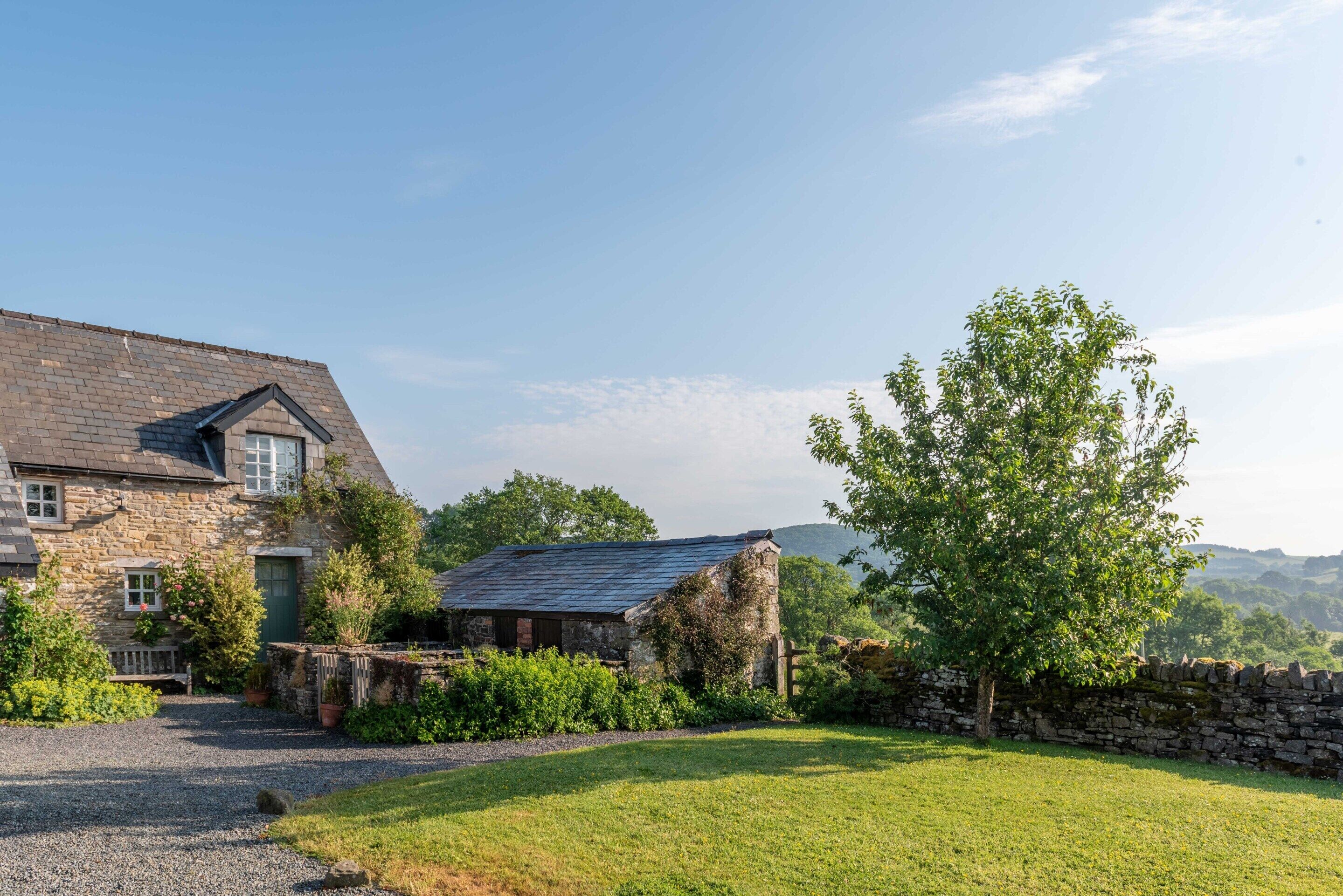 A stone house with a sloped roof, a small outbuilding, and a well-maintained lawn.