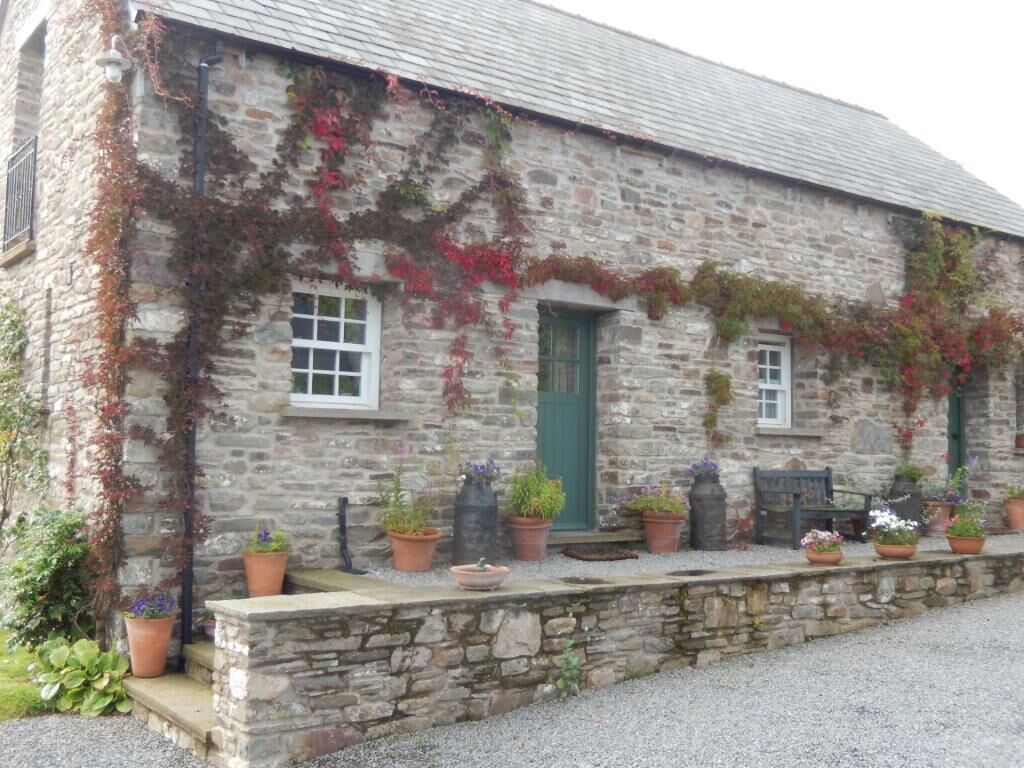 A stone building with a green door, windows, and potted plants along the front.