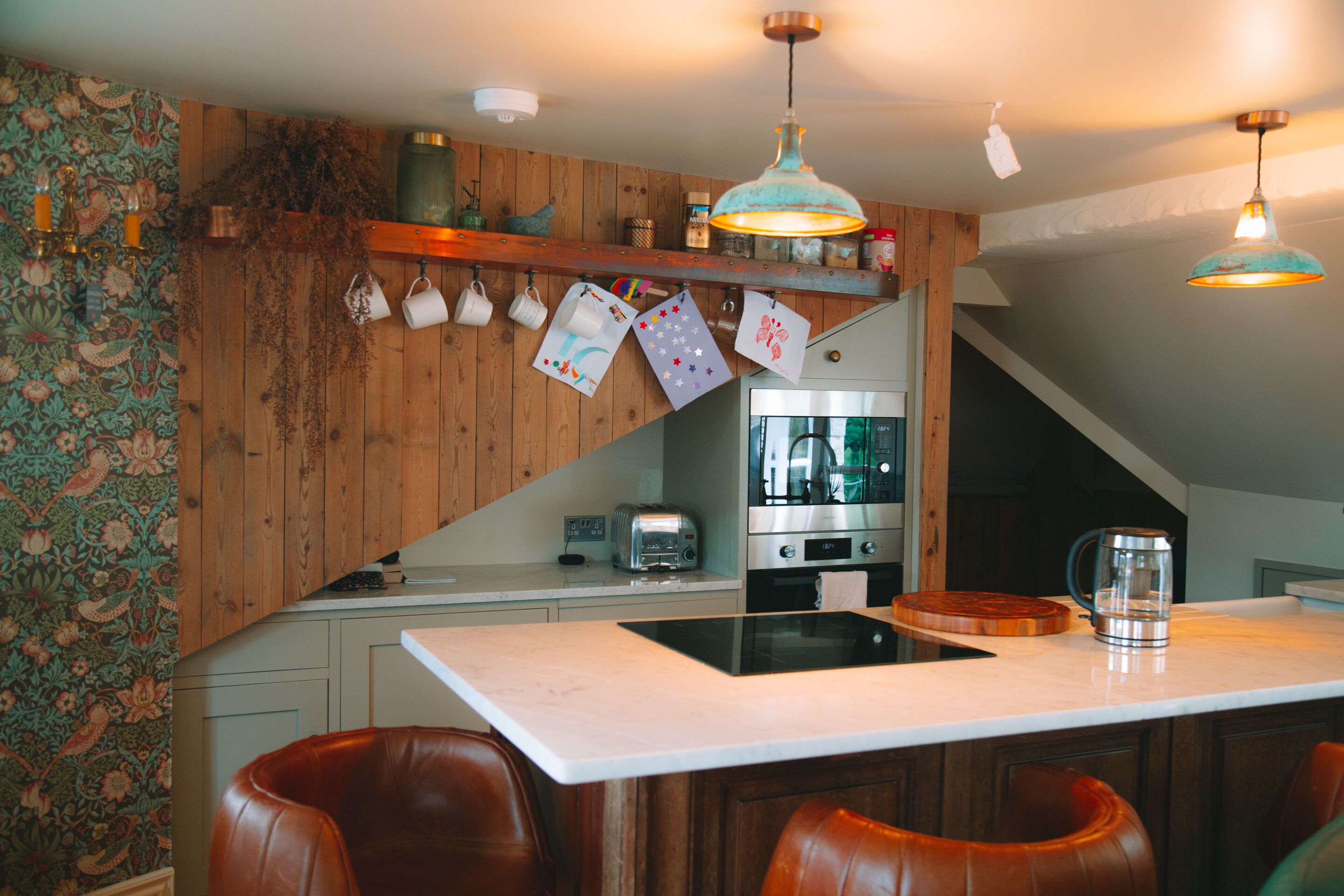 A kitchen with wooden walls, a central island, and a hanging light fixture.
