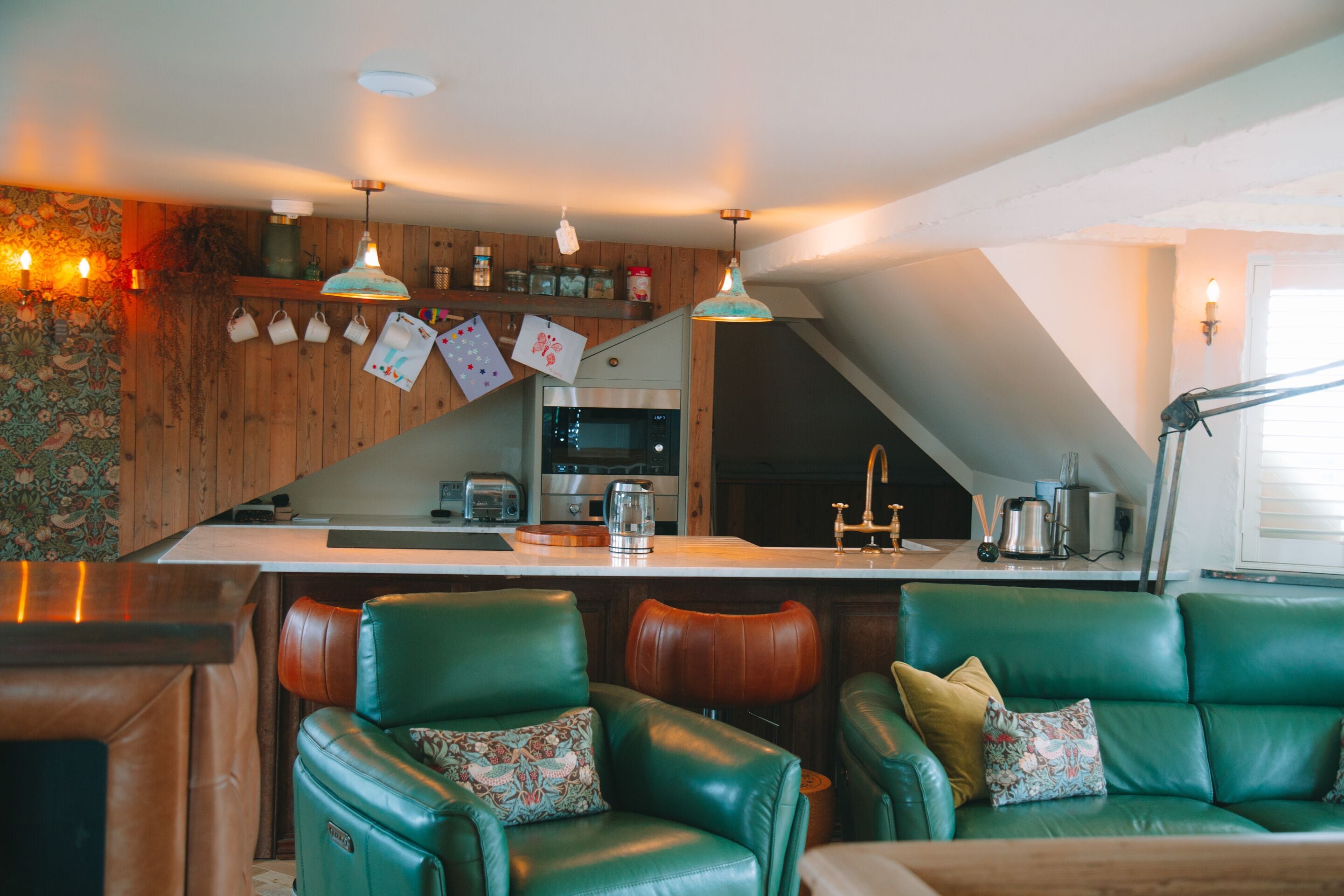 A kitchen with a bar area, green leather chairs, and pendant lighting.