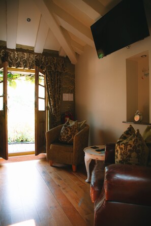 A cozy room with a wooden floor, a brown leather sofa, a patterned armchair, and a flat-screen TV mounted on the wall. - Bradleigh Lodge (St Austell)