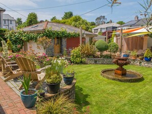 A well-maintained garden with a fountain, potted plants, and outdoor furniture. - Bradleigh Lodge (St Austell)