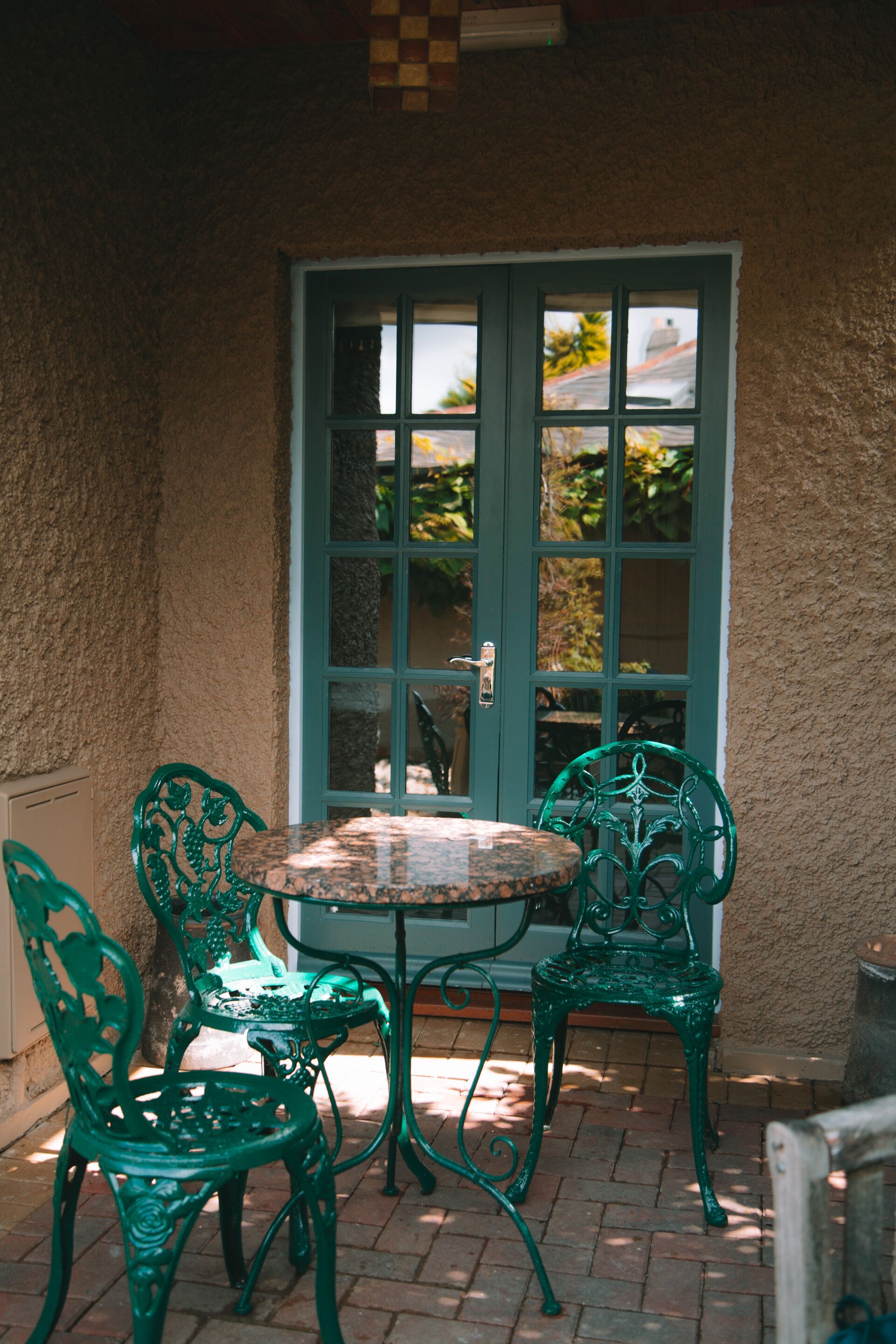 Um pátio com mesa, cadeiras, uma porta e vista para o verde.
