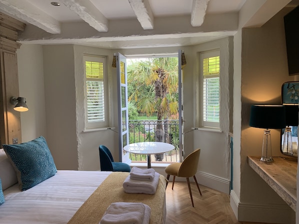 A bedroom with a bed, a small round table, a chair, and a balcony with a view of greenery. - Bradleigh Lodge (St Austell)