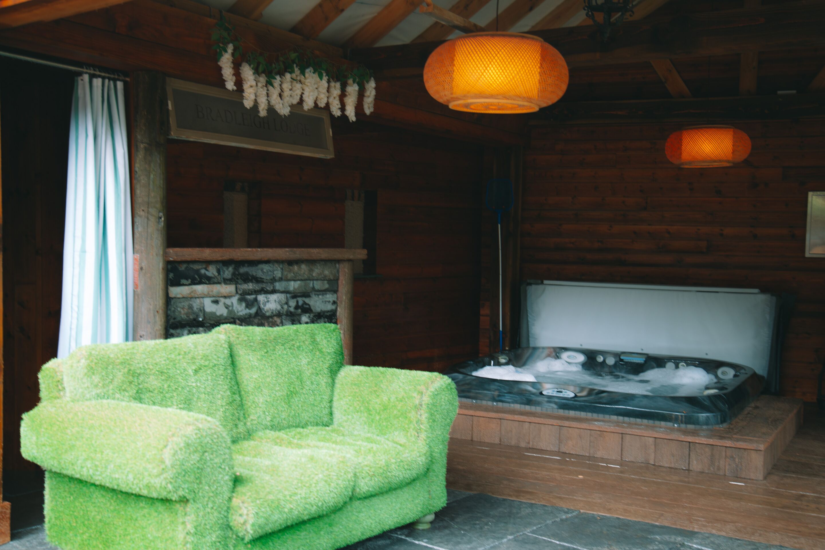 A wooden cabin interior with a green chair, a hot tub, and a hanging light fixture.