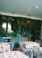 Un restaurante con una pared verde decorada con plantas y flores, una máquina de café y mesas con manteles florales.