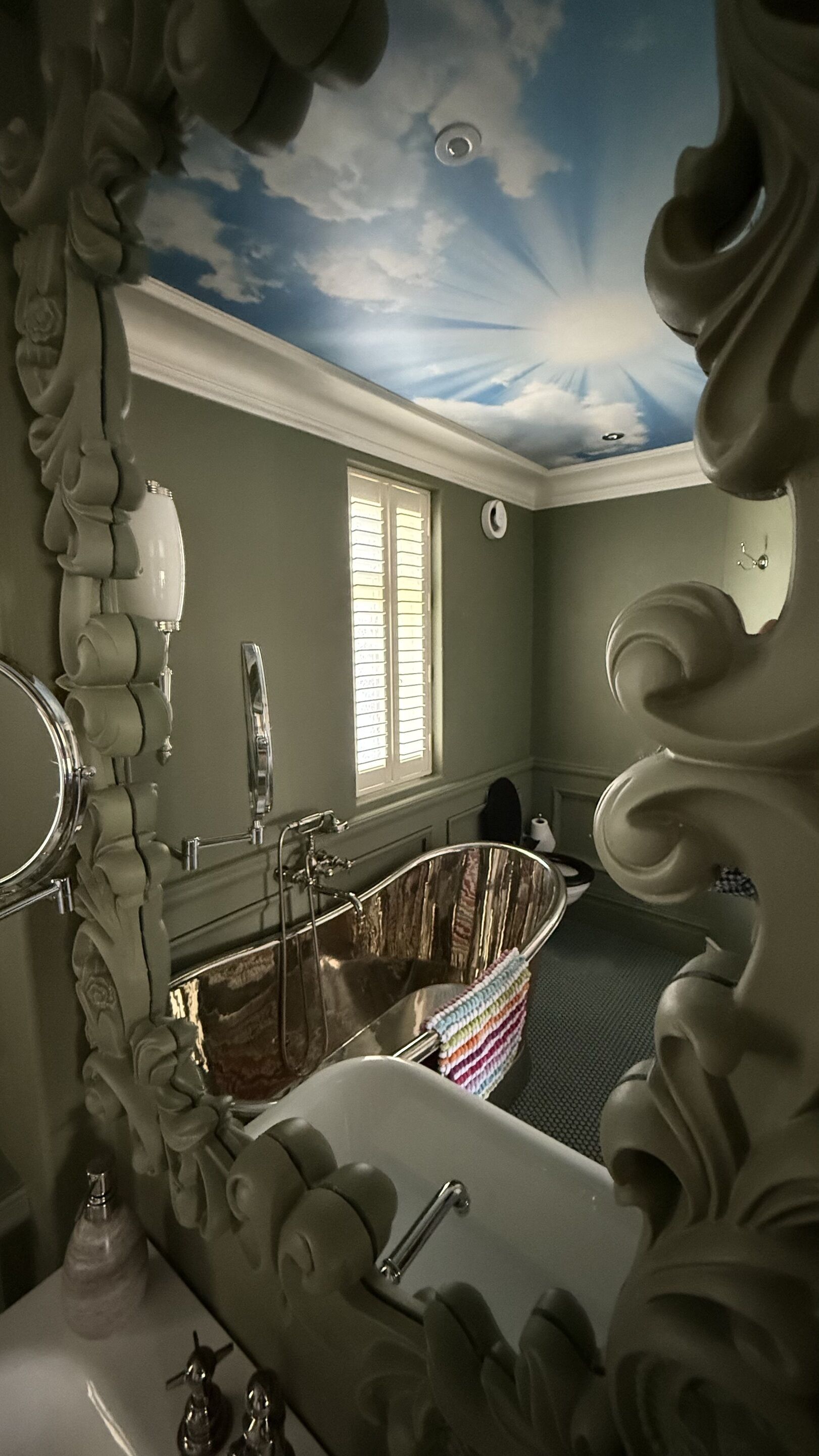 A bathroom with a bathtub, a mirror, a window with blinds, and a ceiling with a sun design.