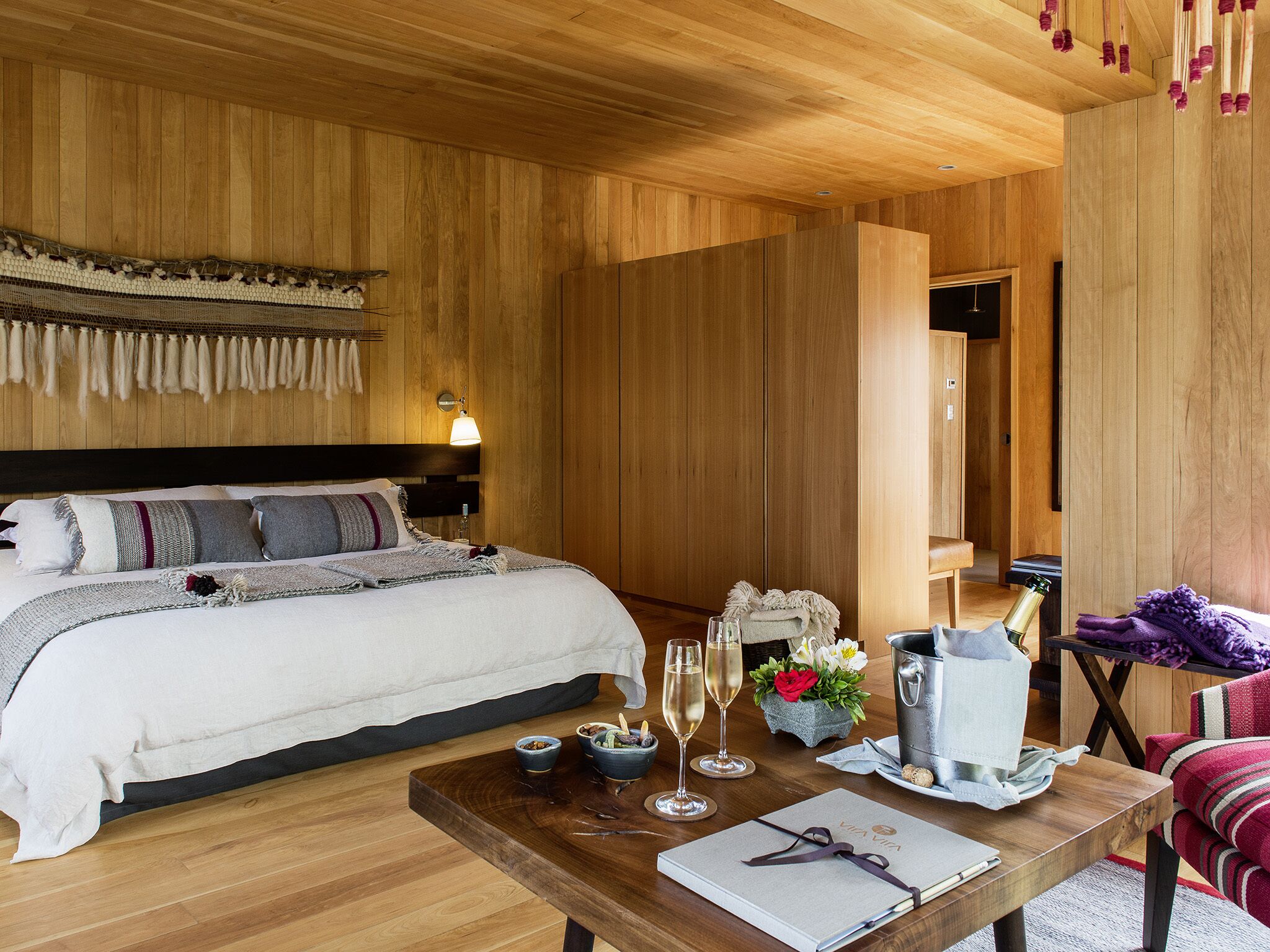 A wooden-themed bedroom with a bed, bedside table, and a small seating area with a table and chairs.