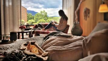 A cozy room with a bed, a table with a vase and a cup, and a view of greenery and mountains.