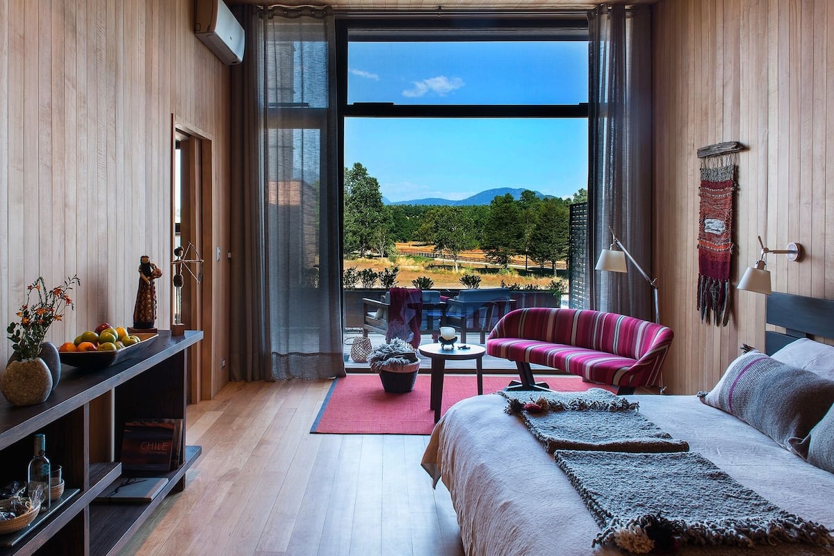 Una habitación moderna con un ventanal grande, una cama, un sofá y una pequeña mesa.