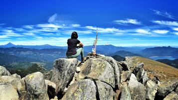 Una persona sentada sobre un saliente rocoso con vista a un paisaje montañoso bajo un cielo despejado.