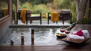 Un tranquilo comedor al aire libre con terraza de madera, una piscina pequeña y una mesa dispuesta con ensalada, bebidas y toallas.