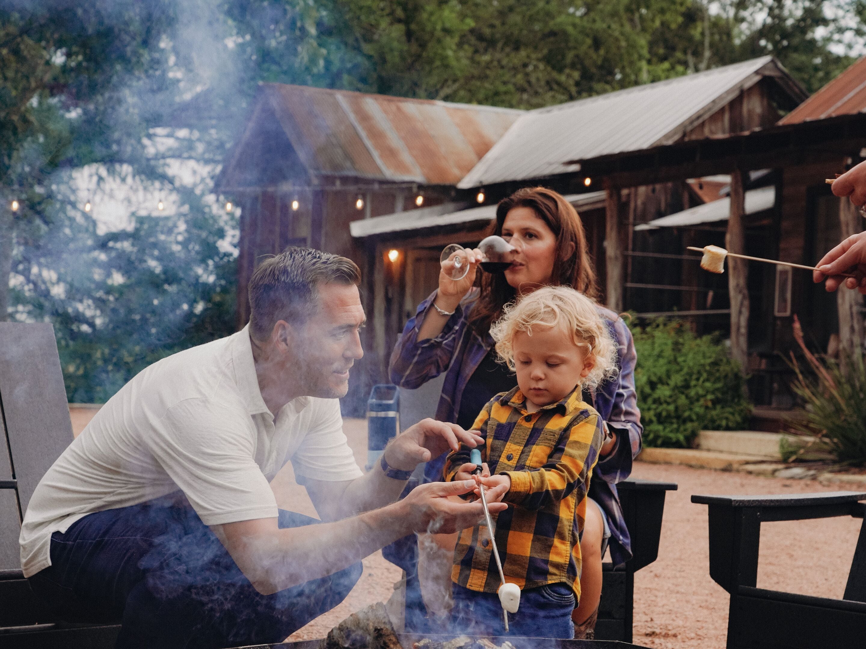 Una familia cocinando al aire libre, con una parrilla y un niño asando malvaviscos.