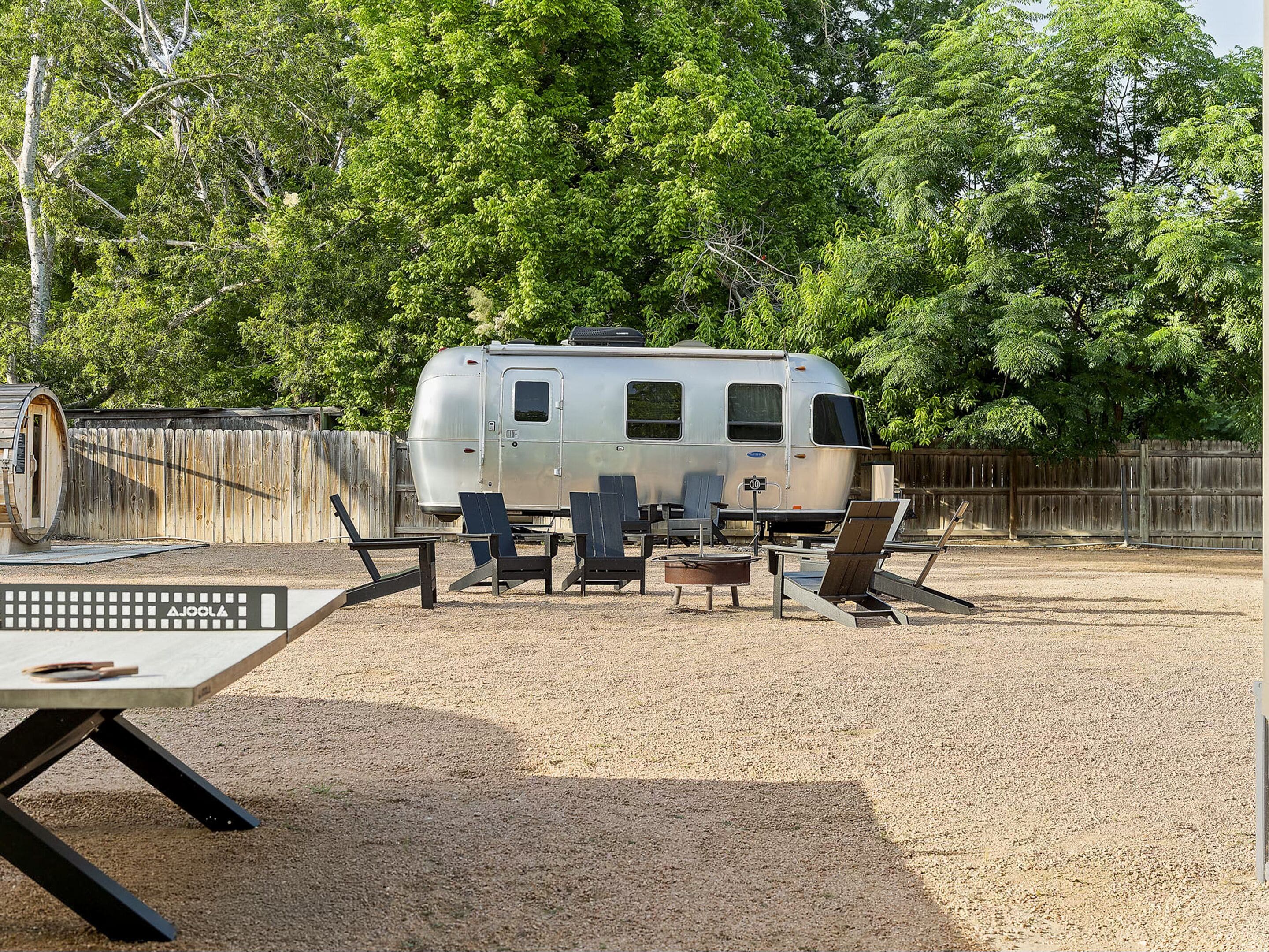 Una caravana estacionada en un camping con mesas de picnic y zona de barbacoa.