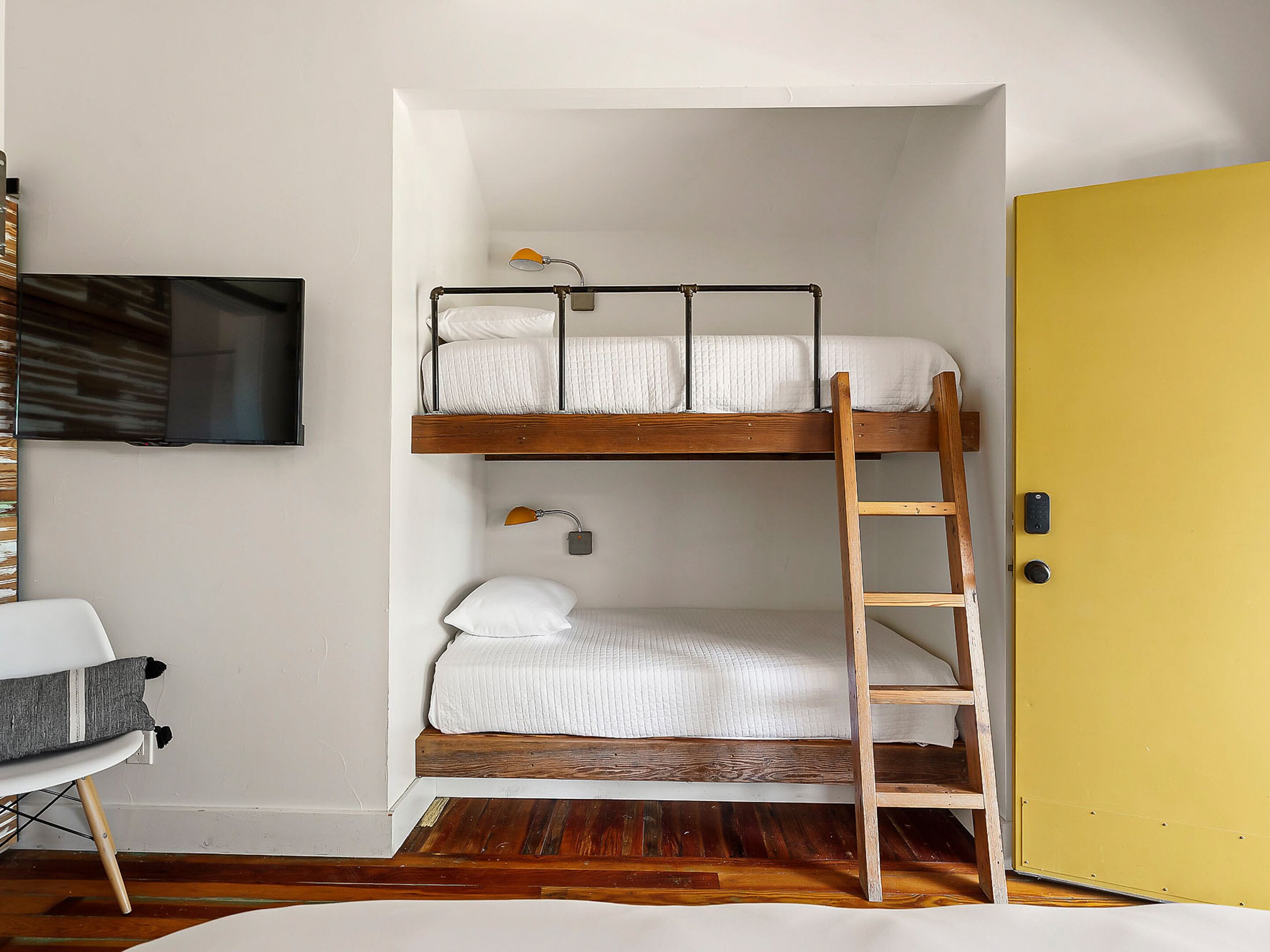 A bunk bed room with a wooden ladder, a television mounted on the wall, and a yellow door.