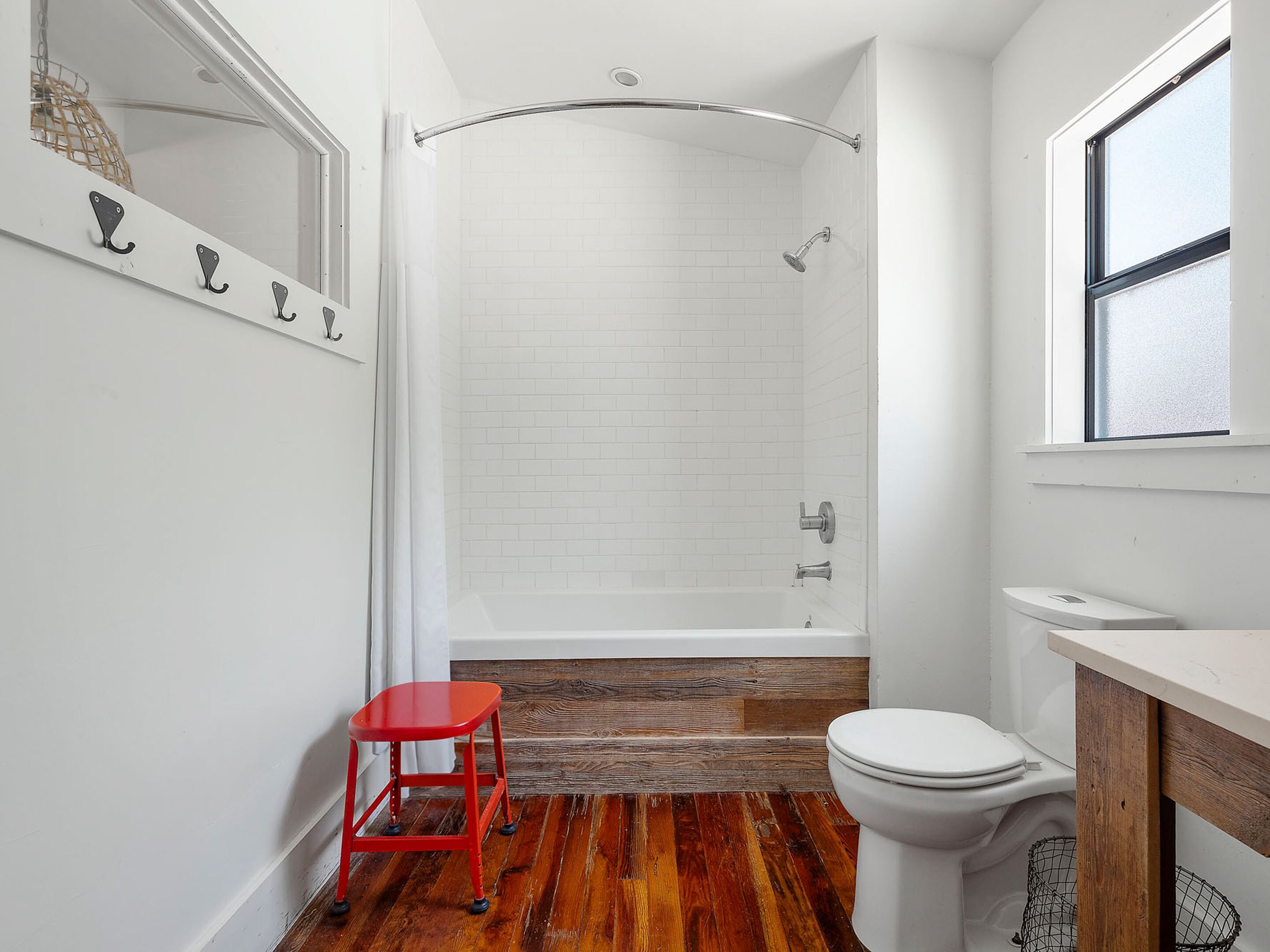 A bathroom with a shower, toilet, and a red stool.