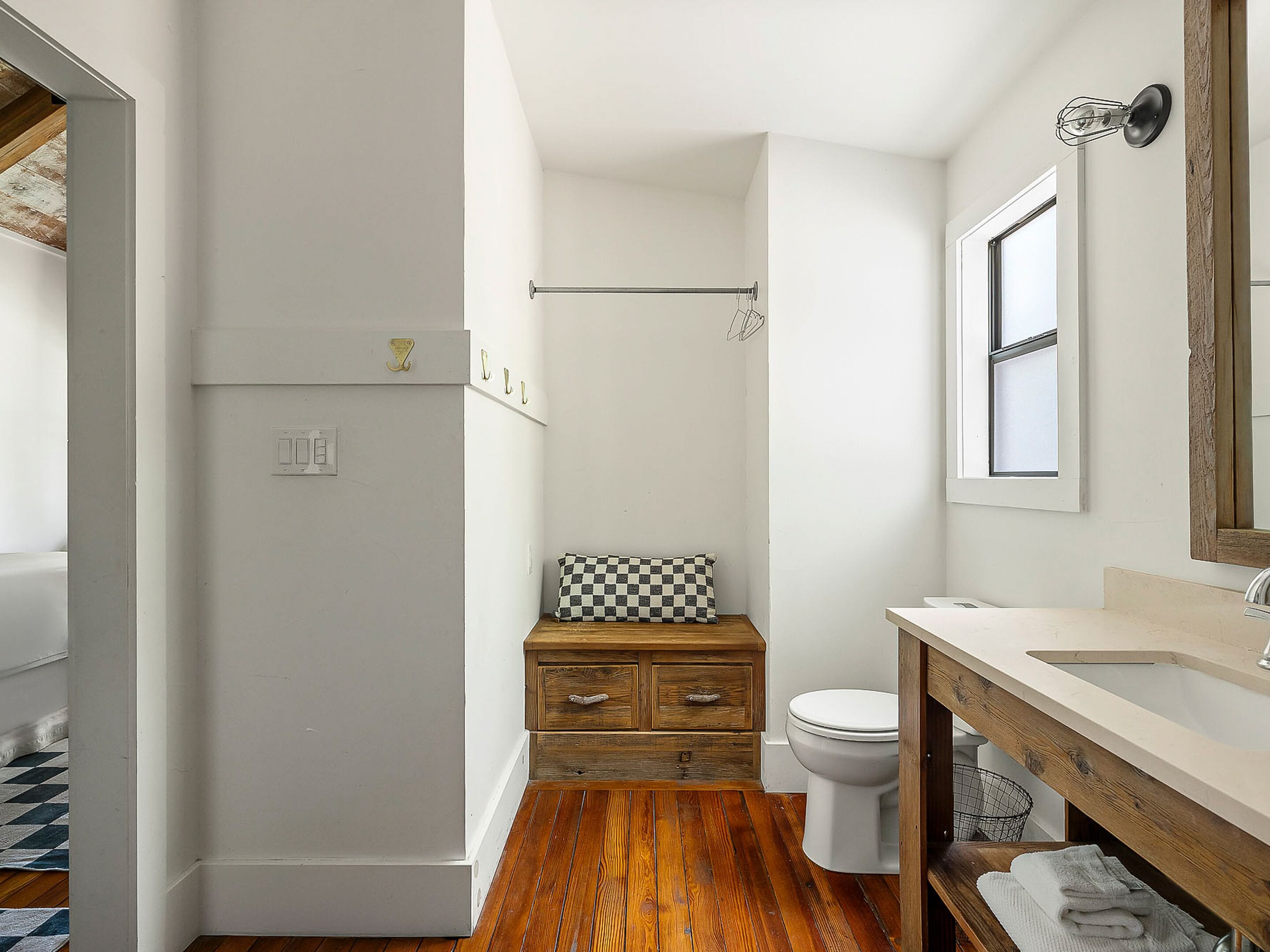 Een compacte badkamer met een houten wastafel, toilet en een klein bankje met een geruit kussen.